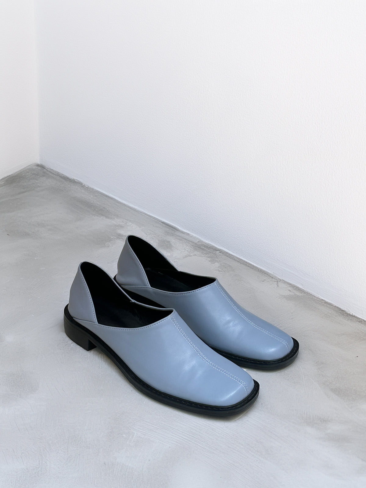 Pair of light blue shoes with black soles on a gray surface.