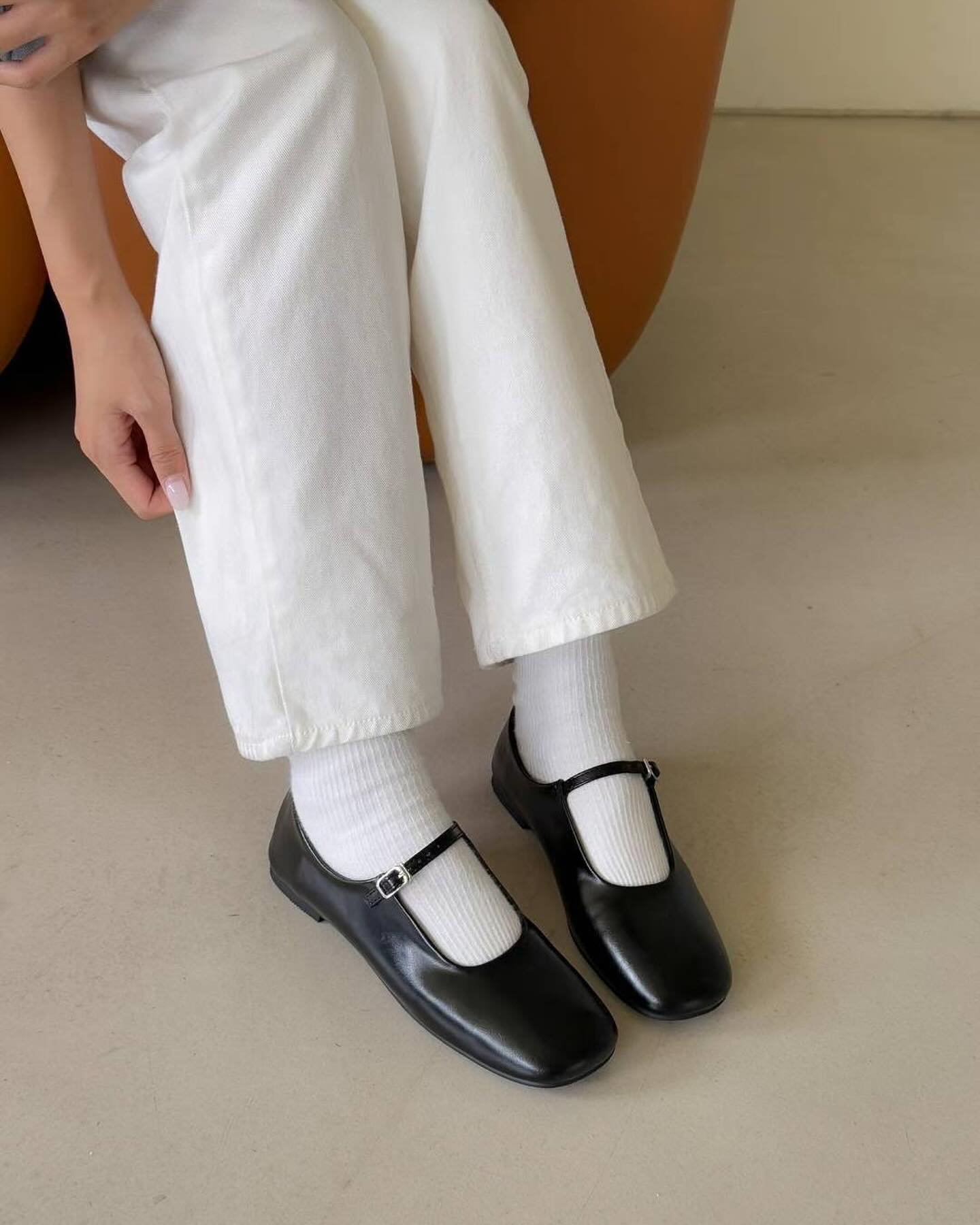 Person wearing black shoes and white pants sitting on a beige chair.